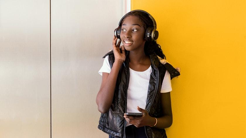 A teenage girl standing against a wall listening to headphones
